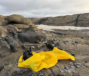 A yellow bivvy bag sits in a rocky landscape