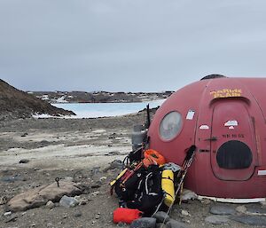A walking pack leans up against a red hut sitting on Antarctic rock