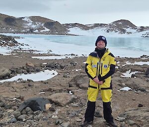 A smiling expeditioner stands in front of a frozen lake