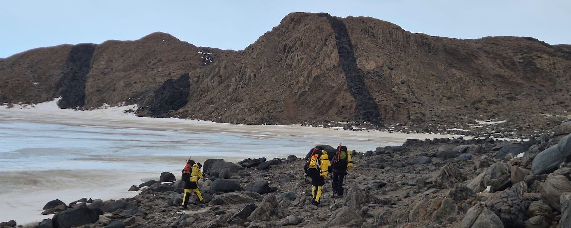 A group of expeditioners in yellor and black survival clothes walk alongside a frozen lake