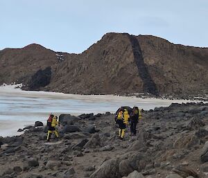 A group of expeditioners in yellor and black survival clothes walk alongside a frozen lake