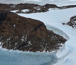 A rock knoll emerges from a frozen lake and is skirted by a shelf of snow