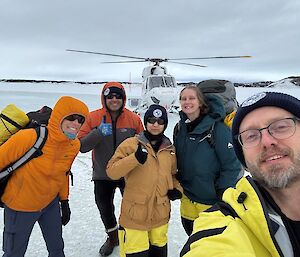 A group of smiling expeditioners standing with a helicopter in the background
