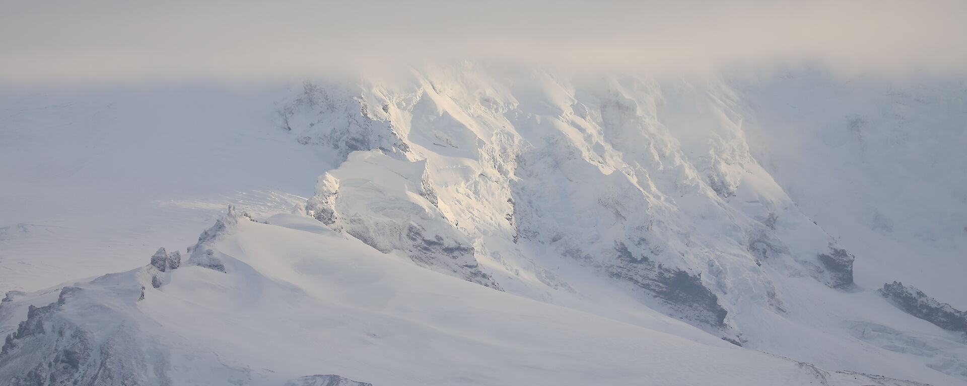 A snow covered mountain, topped in cloud