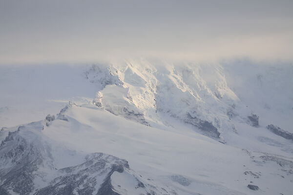A snow covered mountain, topped in cloud