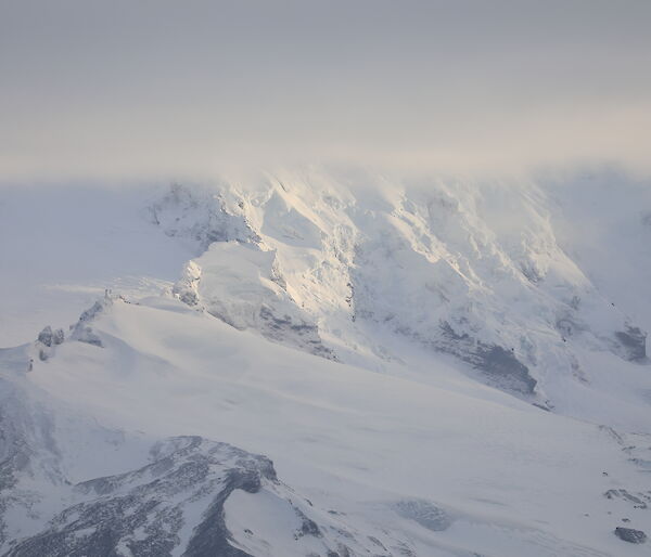 A snow covered mountain, topped in cloud