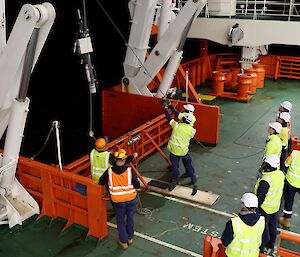 A group of people in high vis watch an Argo float going over the side