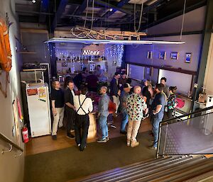 A group of people standing around small bar tables, lit by blue fairy lights