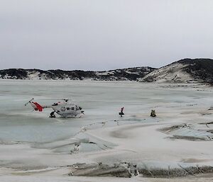 A helicopter parked on sea ice with three people walking away from it carrying bags