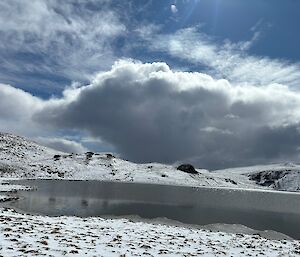 A dark cloud is reflected back from the mirror like surface of a lake set into a snow-covered landscape.