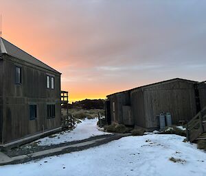 Orange and yellow streaked cloudy sky as the sun rises over buildings set in a snow-covered landscape.