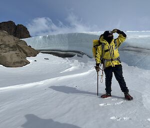 An expeditioner in yellow with an ice cliff behind him