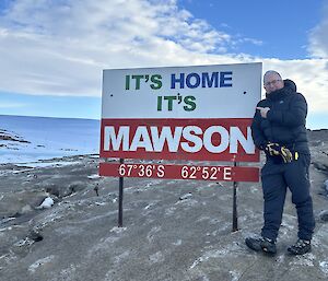A sign saying 'It's home, it's Mawson' on a rock with a man standing next to it