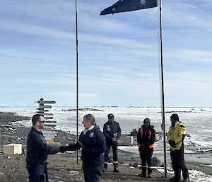 A man shakes a woman's hand, standing in front of a raised Australian flag
