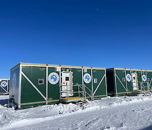 Four green shipping containers in a row on the snow.