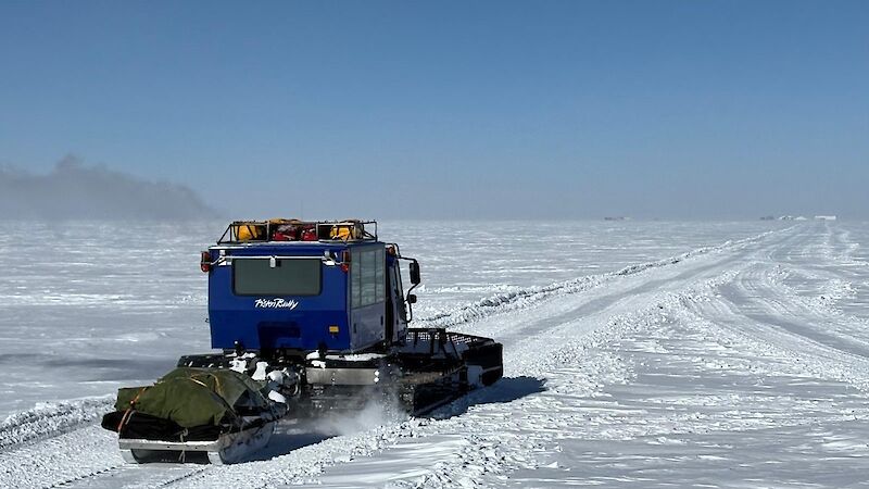 A snow tractor makes its way across a snowy plain