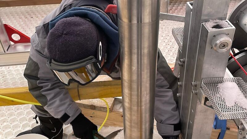 A person in goggles measures the base of a metal tube.