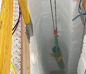 A piece of green pipe being lowered into a deep ice hole