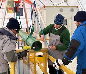 Three people working with a green pipe