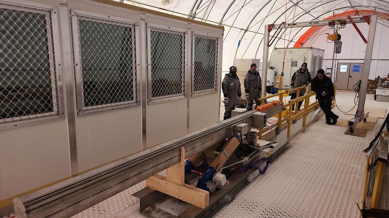 A group of people stand around a long silver pipe inside a white tent
