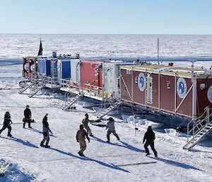 A group of people playing volleyball on snow in front of several shipping containers
