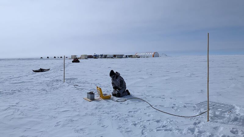 A person crouched over equipment in the snow