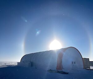 A perfectly round rainbow in a blue sky over a tubular tent