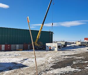 A crane is fixed to a white temperature controlled container sitting in front of a large green building with a bright blue sky behind.