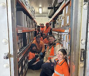 11 expeditioners wearing high visiblity clothing pose for a photo inside a cramped refrigeration space