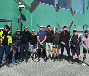 A group of ten people in athletic wear stand in a line in front of a green building