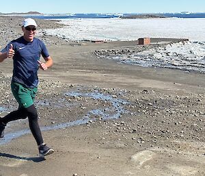 A runner gives a thumbs up to the camera whilst running up a path in front of sea ice
