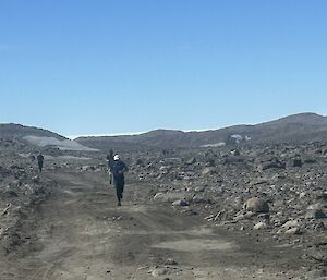 A group of expeditioners run towards the camera, up a slight incline in a roacky landscape