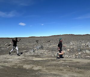 Two expeditioners run along a dirt road, left to right of screen. The second expeditioner has both arms raised in celebration