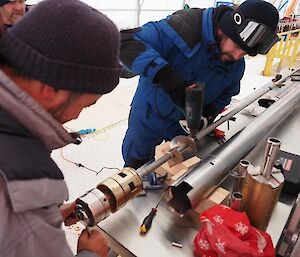 Two men working on a long metal pipe