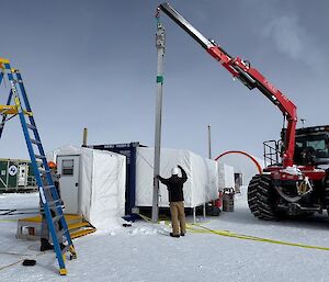 A crane installing a tall metal pole on a snowy slope