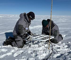Two people with a scientific instrument on the snow surface.