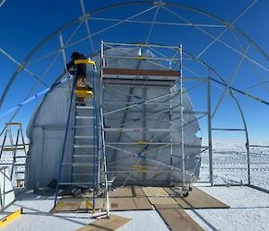 A man installs covers on the arched ends of a steel-framed tent.