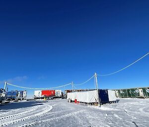 A field camp of shipping containers. Power cables run across the site from the generotor to a mess tent and on to a drilling shelter.