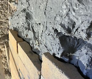 Cream coloured bricks at the base with grey mortar above it on the wall of an incinerator