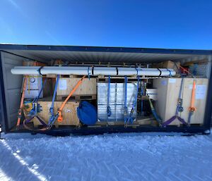 A shipping container neatly packed with boxes and pipes, all tied down tightly to tie points at the base of the container.