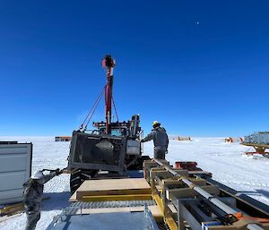 The tractor uses its crane to load a winch onto a sled.