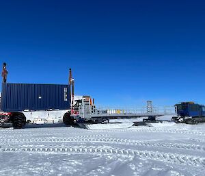 A shipping container being unloaded near the drilling shelter using cranes on two tractors.