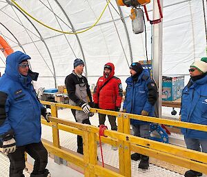Five people stading beside a wooden framework used to guide the ice core drill barrel.