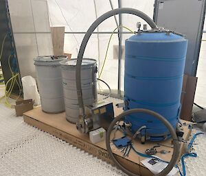 A large blue drum and two smaller 44 gallon drums connected to pipework that will form part of a drill fluid recovery system for the million year ice core drilling effort.