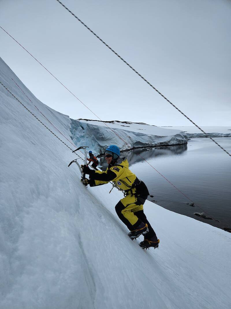 A woman wearing crampons and carrying two ice axes climbing a steep, icy slope in Antarctica