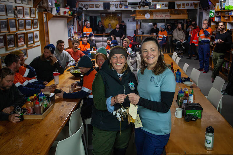 Two women exchange ceremonial keys to Macquarie Island research station while people in the background look on.
