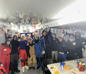 A group of people inside a small dining area, around plates of snacks on a table.