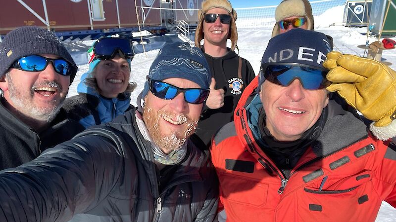 A group of people posing for a selfie in front of shipping container accommodation vans.
