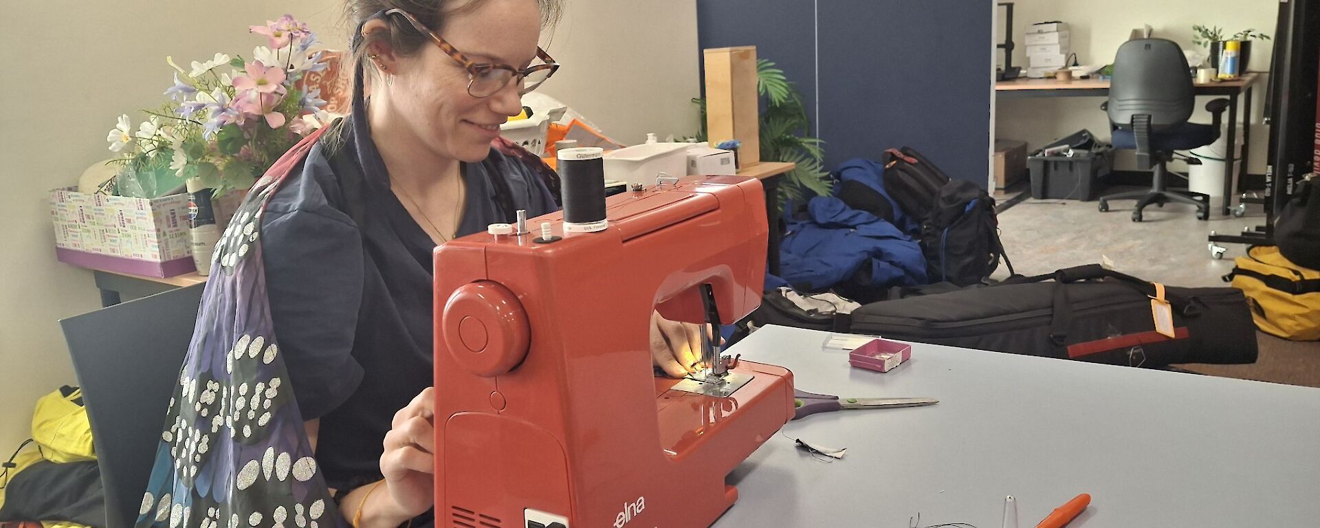 Lisa at the sewing machine, conducting her fix it fairy magic in the foreground, the lower lounge area in the background