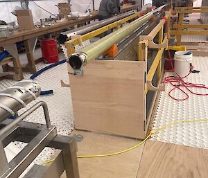 Wooden trapdoors in the floor and entry to the ice coring trench. The ice core drill barrel is lying horizontally on a metal scaffold above the trench.